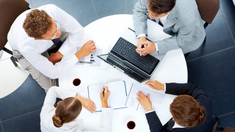 A group of people sitting around a table with laptops.