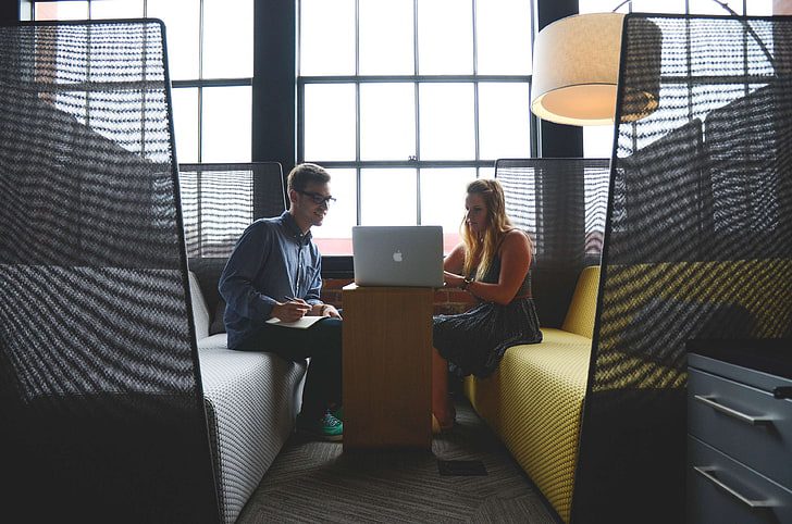 Two people sitting in a booth with one of them using a laptop.