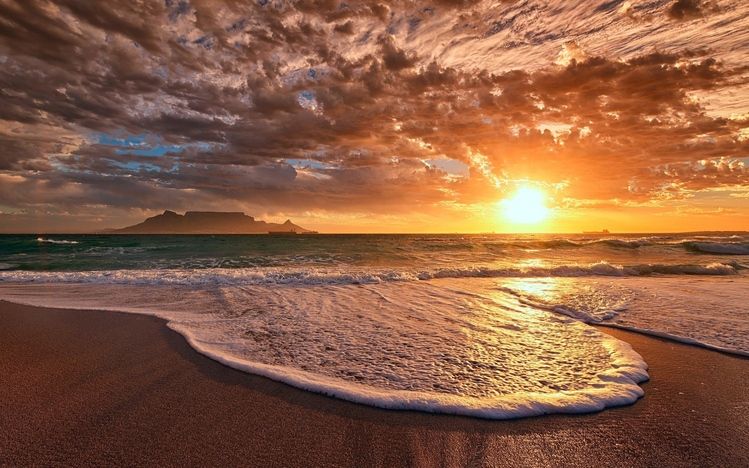 A sunset over the ocean with waves coming in.