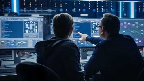Two people sitting in front of computer monitors.