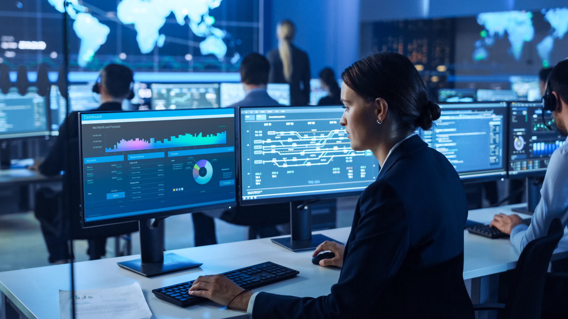 Woman analyzing data on multiple computer screens in a tech workspace.